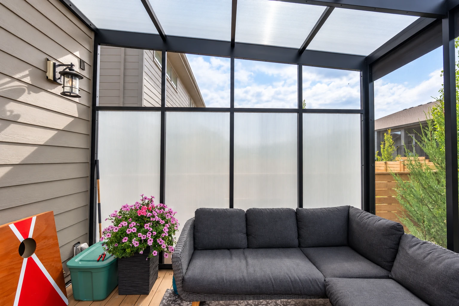Enclosed patio room with a dark metal frame, translucent roof panels, and a large gray sectional sofa.