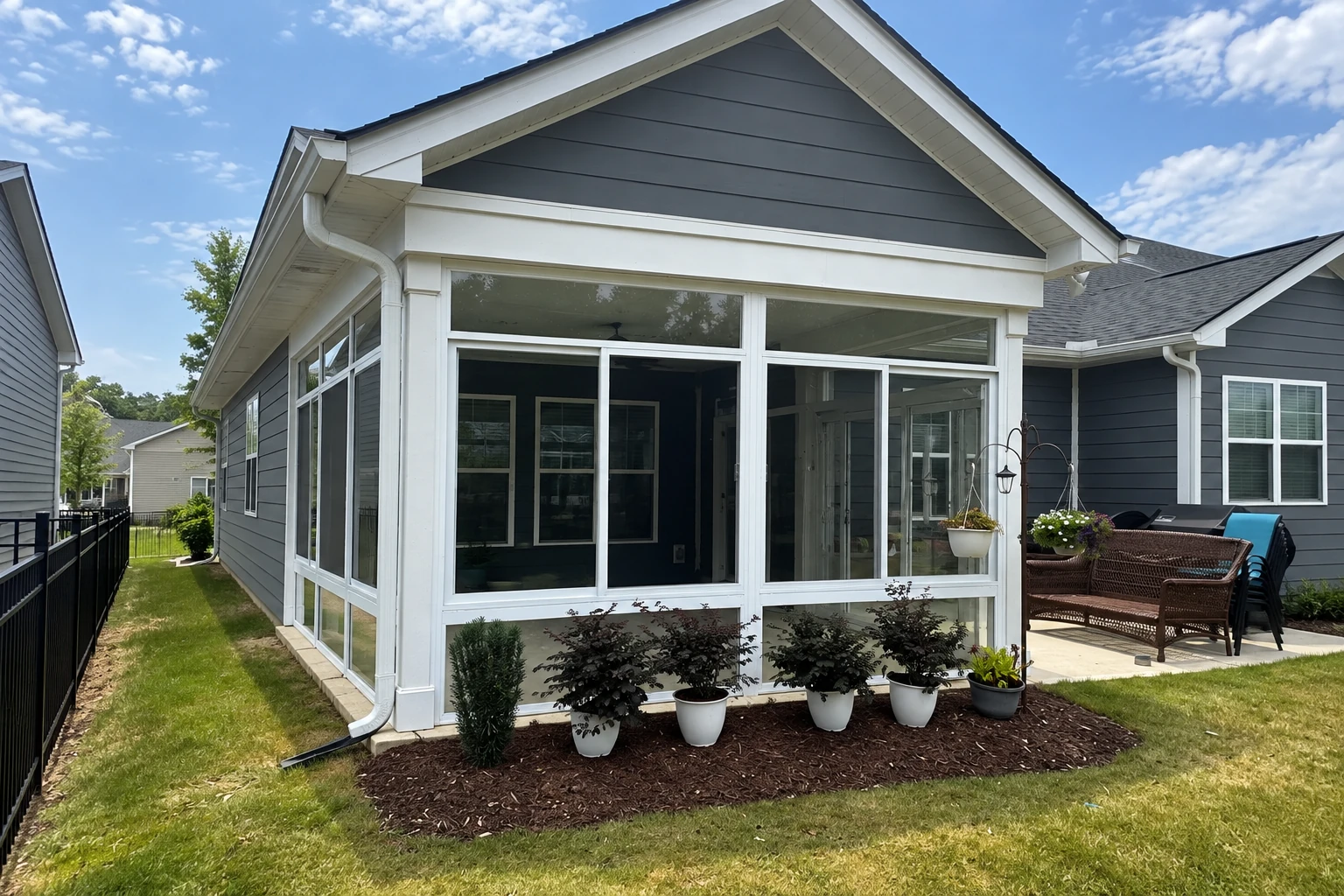 White-framed sunroom addition with a peaked roof and broad windows, attached to a dark-sided house.