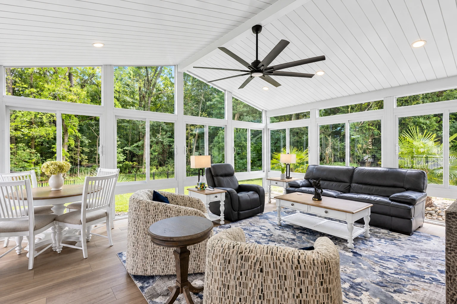 Spacious sunroom with white-framed windows, a vaulted paneled ceiling, ceiling fan, and dining and lounge areas.