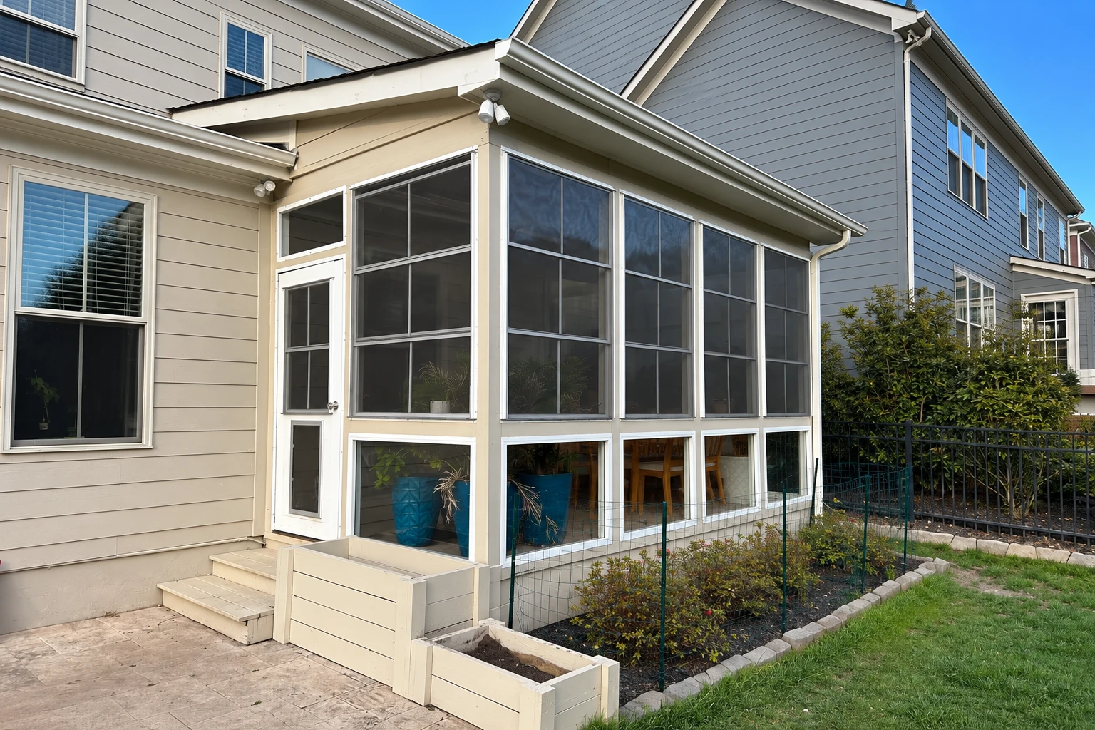 Three-season sunroom with white-framed screened panels and a door attached to a light-sided house.